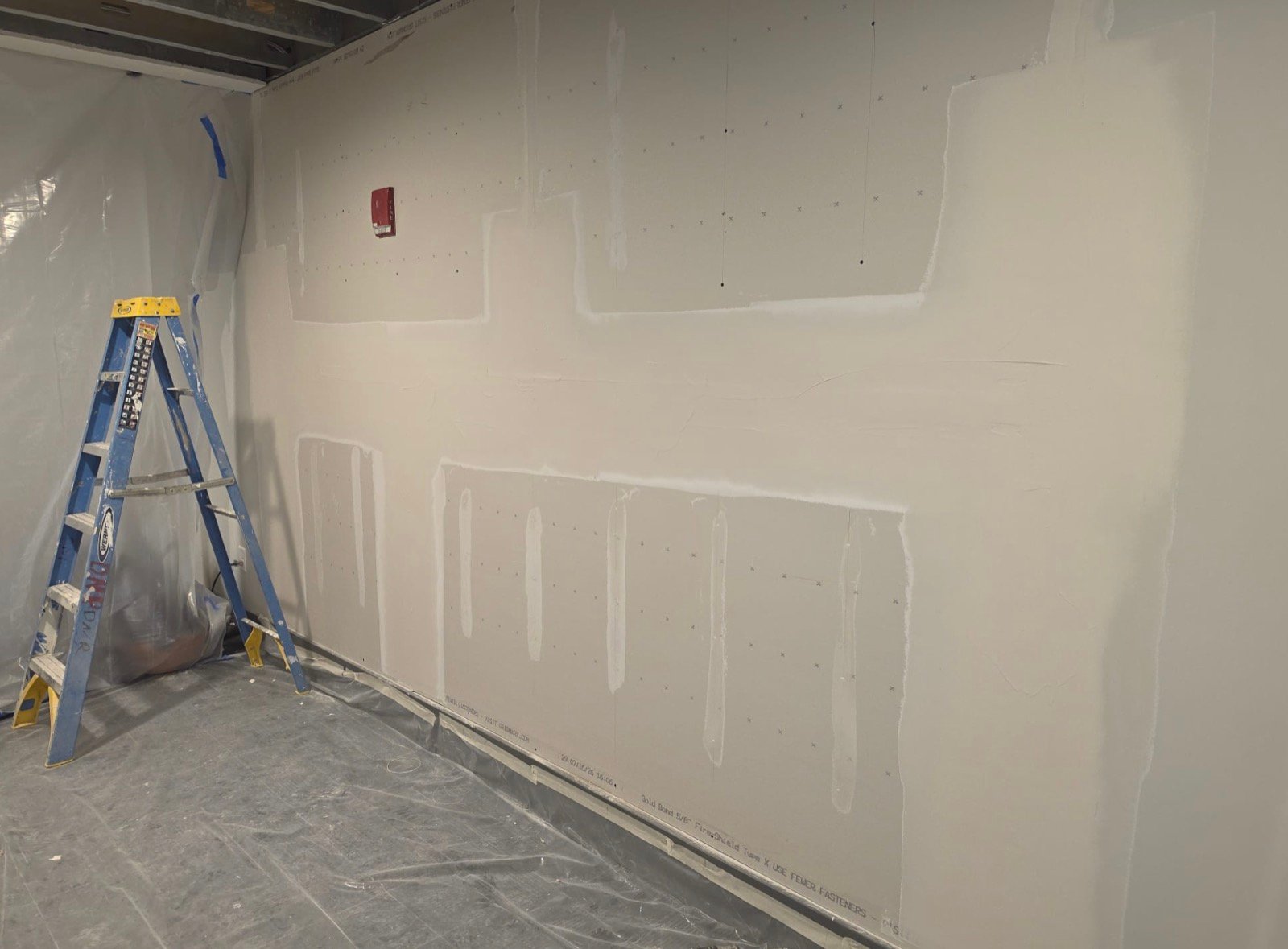 Commercial wall with drywall seams taped and coated, floor and adjacent areas protected with plastic sheeting